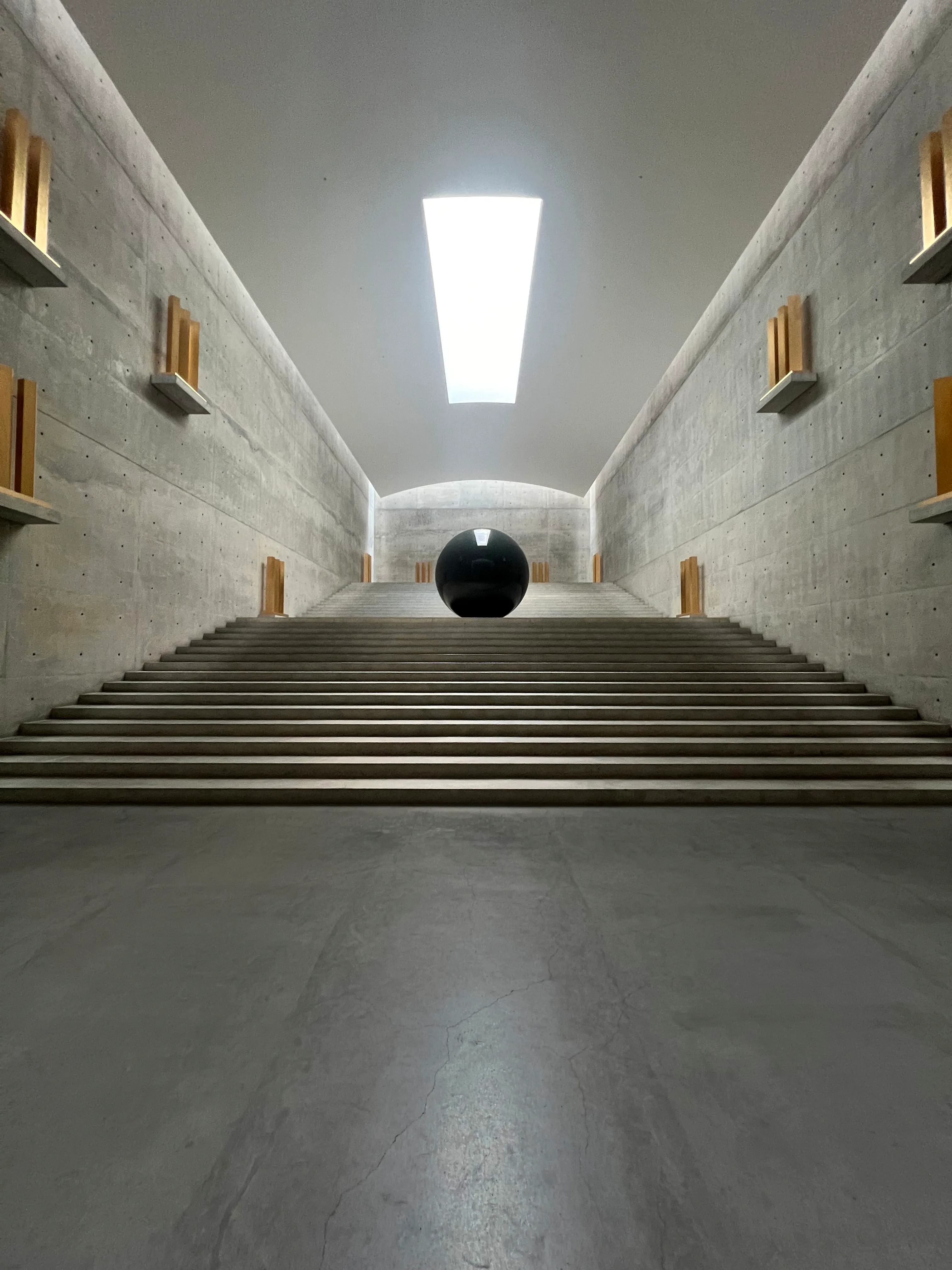 A concrete stair rising to a slit of skylight