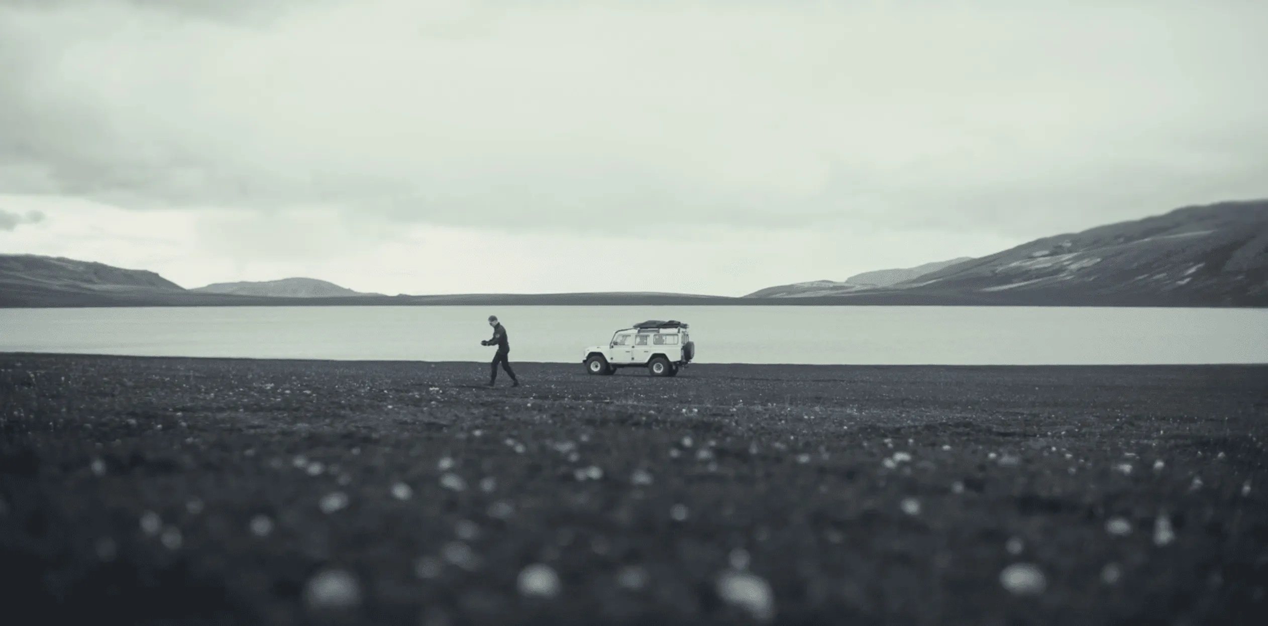 Michael Reed beside a Defender on a black-sand plain in Iceland, under low cloud, on set for the Rhino Rdy opening sequence