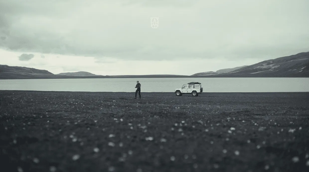 A lone figure and a Defender on a black-sand plain in Iceland