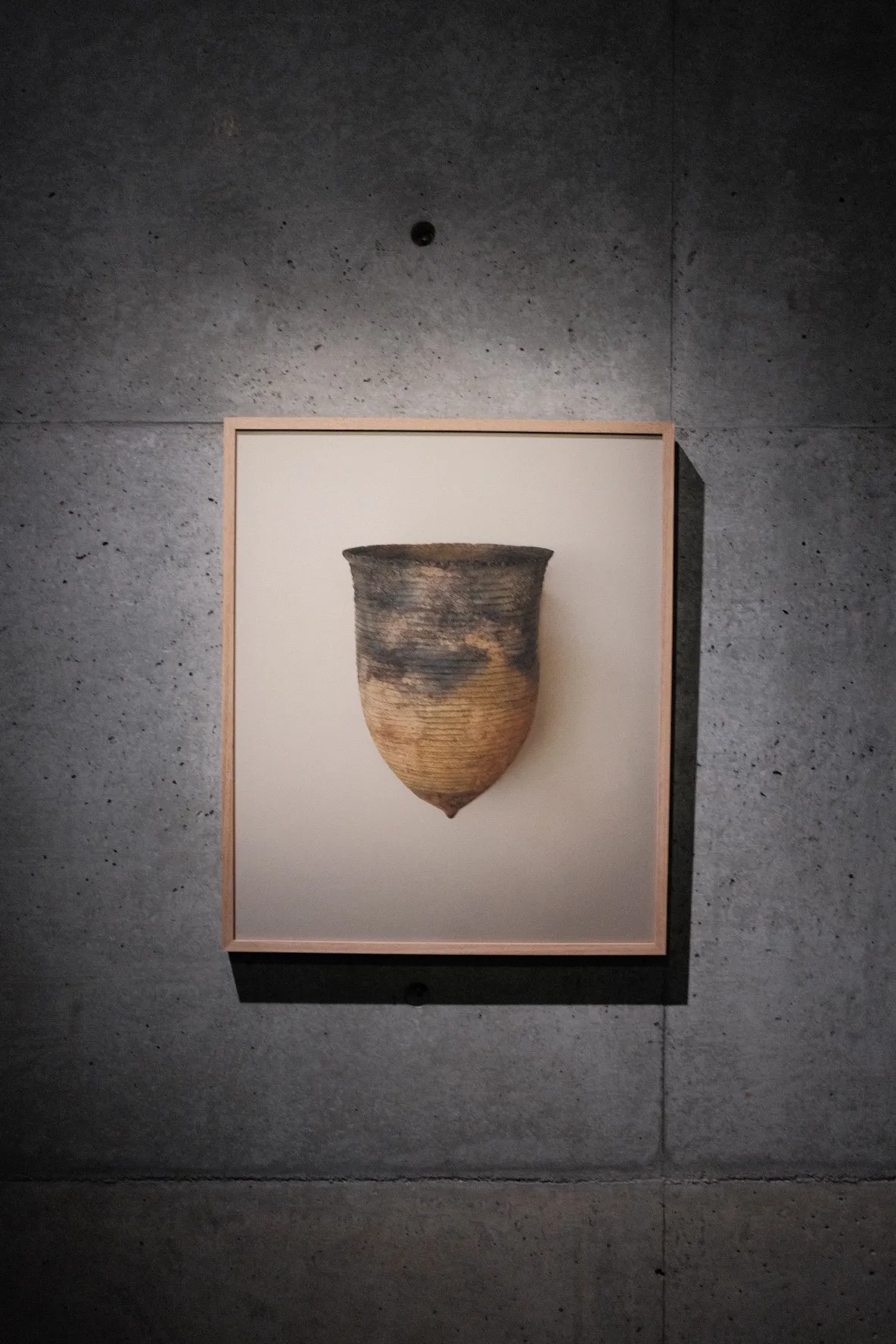 A Jomon-period earthenware vessel, framed on a board-formed concrete wall